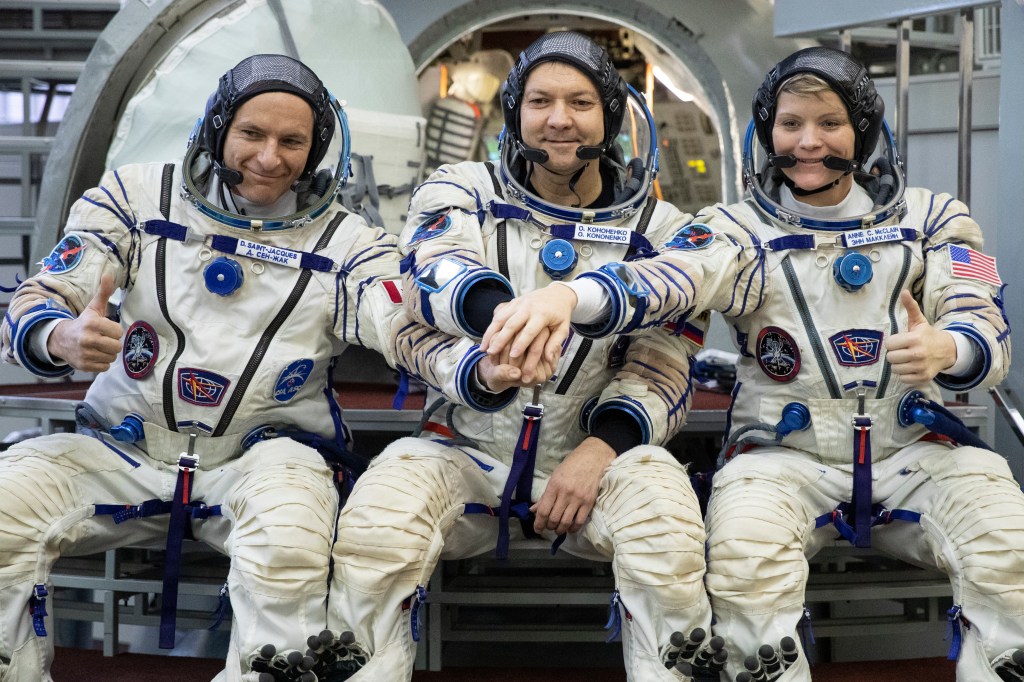 Three astronauts smiling and posing for a photo during preflight training in a Soyuz spacecraft mock-up at Russian Space Training Center.