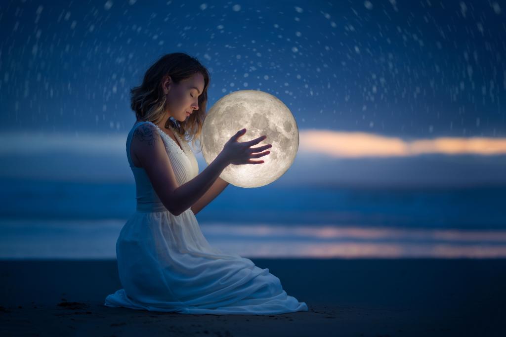 Delicate photography, Astrology, Women's magic. Beautiful attractive girl on a night beach with sand and stars hugs the moon, art photography.