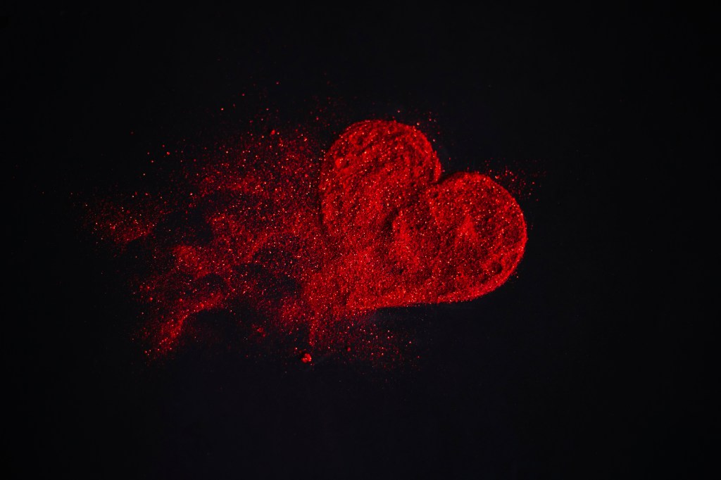 Scattered red heart made of sparkles on a black background. Shimmering dust symbol. Broken love concept