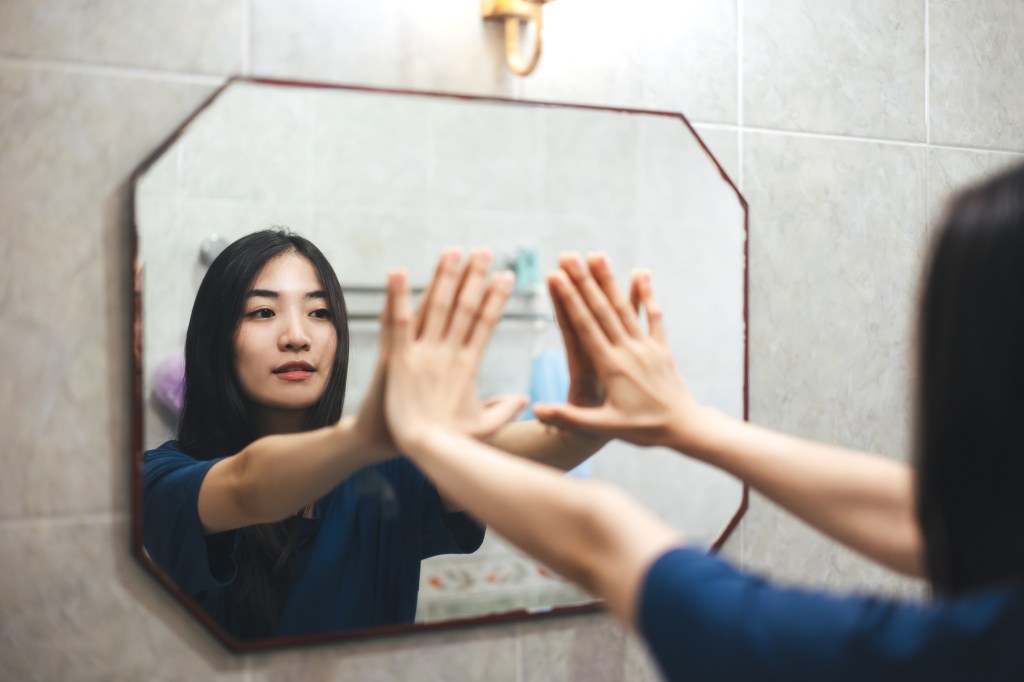 Young adult smile asian woman practice self talk conversation in the morning in bathroom at home.