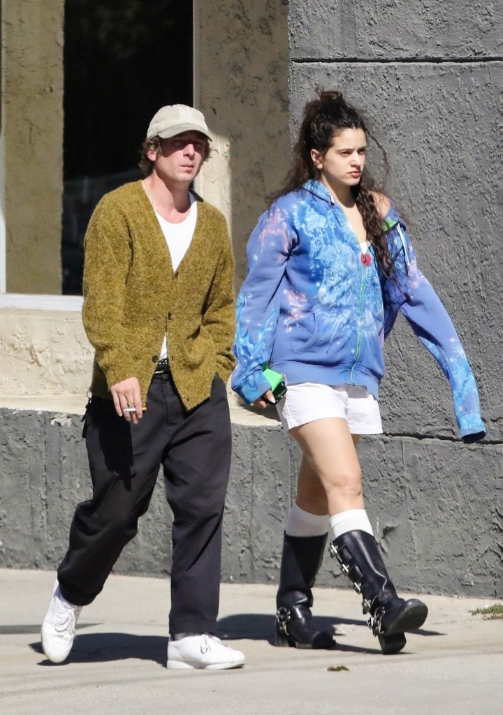 Jeremy Allan White and Rosalia walking on a sidewalk holding flowers