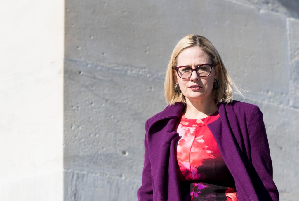 Kyrsten Sinema, a woman in a purple coat, walks down the House steps following the final scheduled votes of the week.