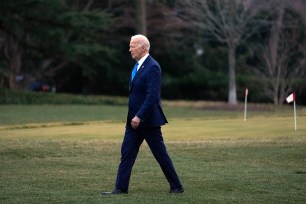 President Joe Biden walks on grass wearing a suit to board Marine One at the White House in Washington.