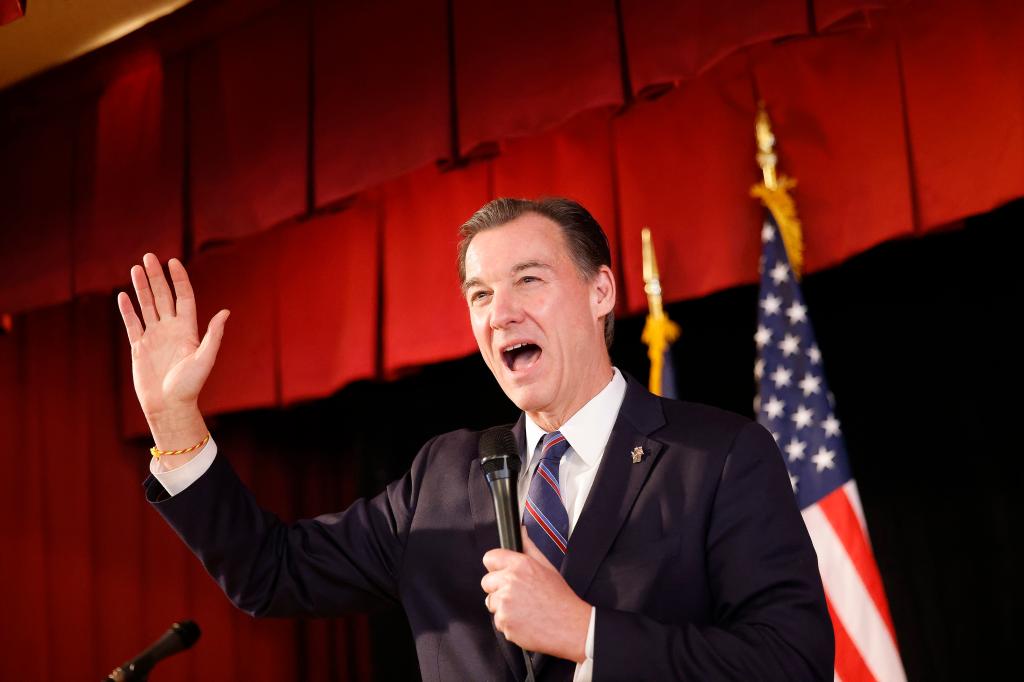 Thomas Suozzi speaking into a microphone at a get out the vote rally at Cove Glen Polish Home, wearing a suit and tie.