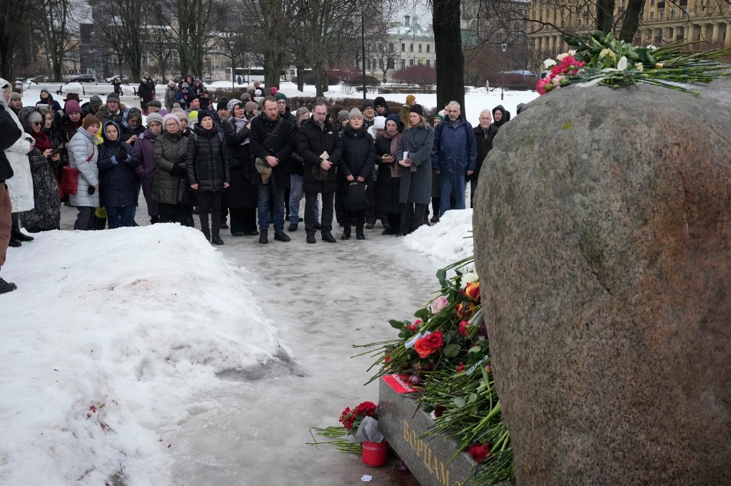 People pray as they come to pay the last respect to Alexei Navalny at the monument, a large boulder from the Solovetsky islands, where the first camp of the Gulag political prison system was established, in St. Petersburg, Russia on Saturday, Feb. 17, 2024. 