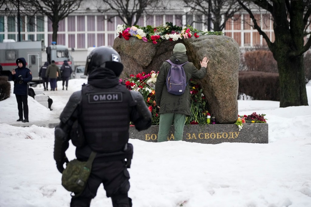 A police officer watches as a man lays flowers paying the last respect to Alexei Navalny at the monument