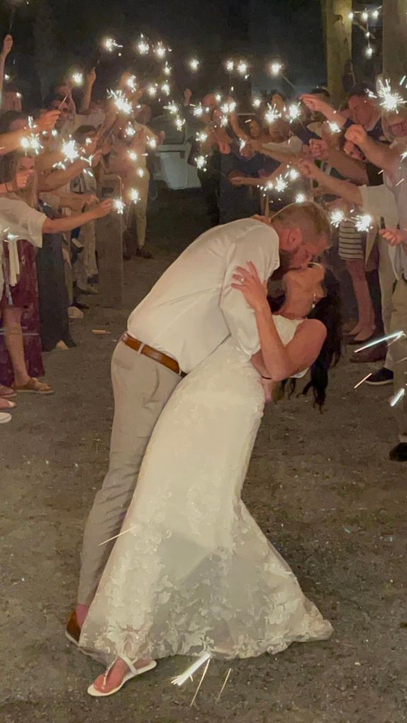 Aric Hutchinson and Samantha Miller kiss on their wedding day while surrounded by loved ones holding sparklers