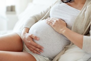 A pregnant woman lying in bed and touching her belly at home.