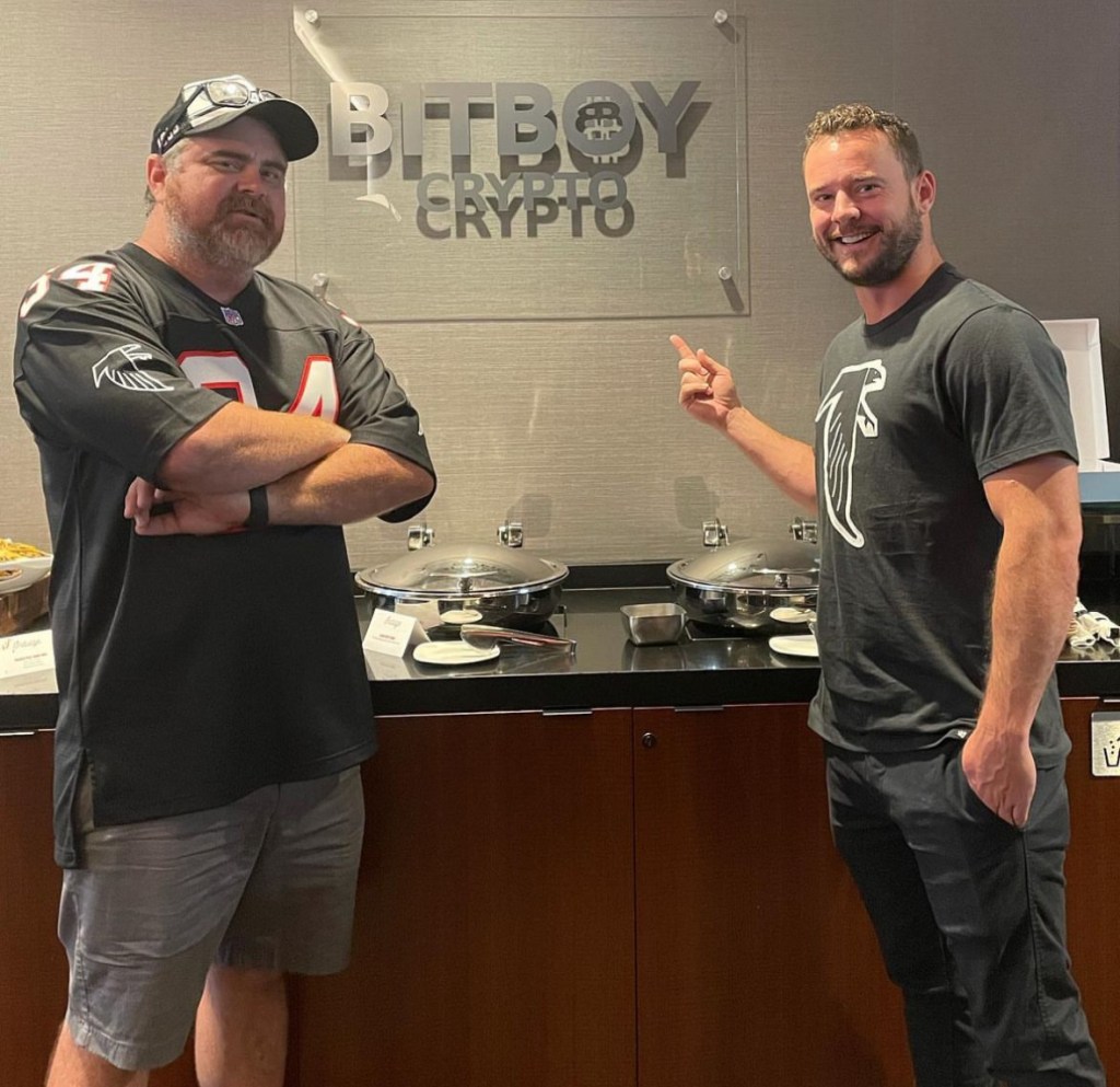 Ben Armstrong with another man, coworker, in front of BitBoy crypto sign.