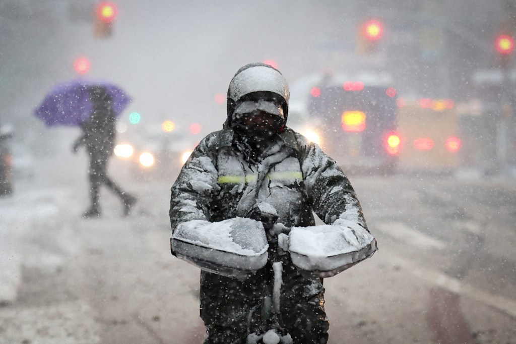 A delivery worker riding a bicycle covered in snow on East 125th Street during winter weather in Manhattan in New York City.