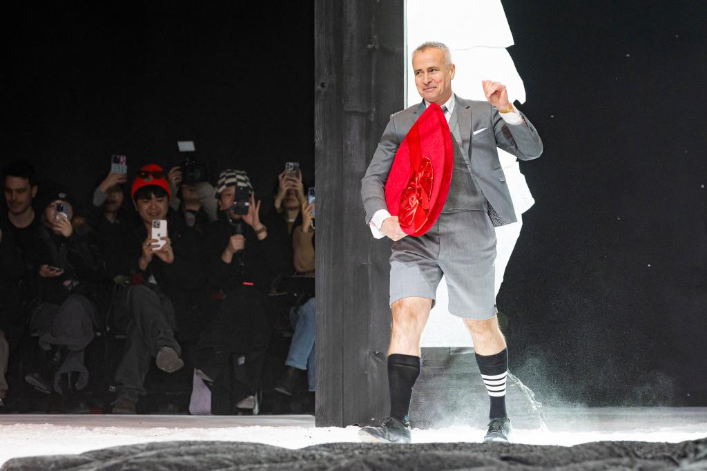 Thom Browne greets attendees at his fashion show, swiftly walking down the runway wearing a gray blazer and pants.