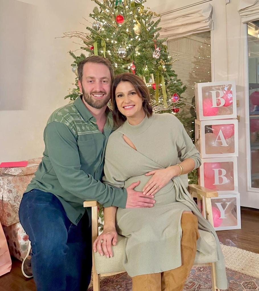 A visibly pregnant Shannon Murray and her husband, Chris, pose in front of a Christmas tree with large stacked clear blocks that spell out "BABY" next to it.