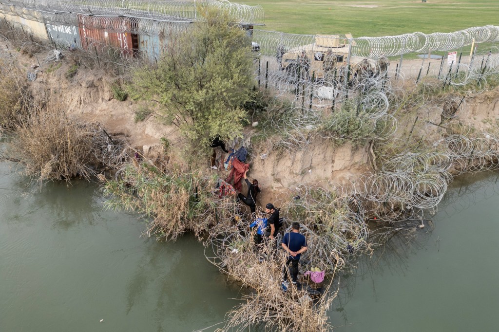A group of migrants attempt to go through a wire fence on the banks of the Rio Grande river as members of U.S. National Guards stand guard on the other side of the fence in Eagle Pass, Texas, U.S., February 27, 2024
