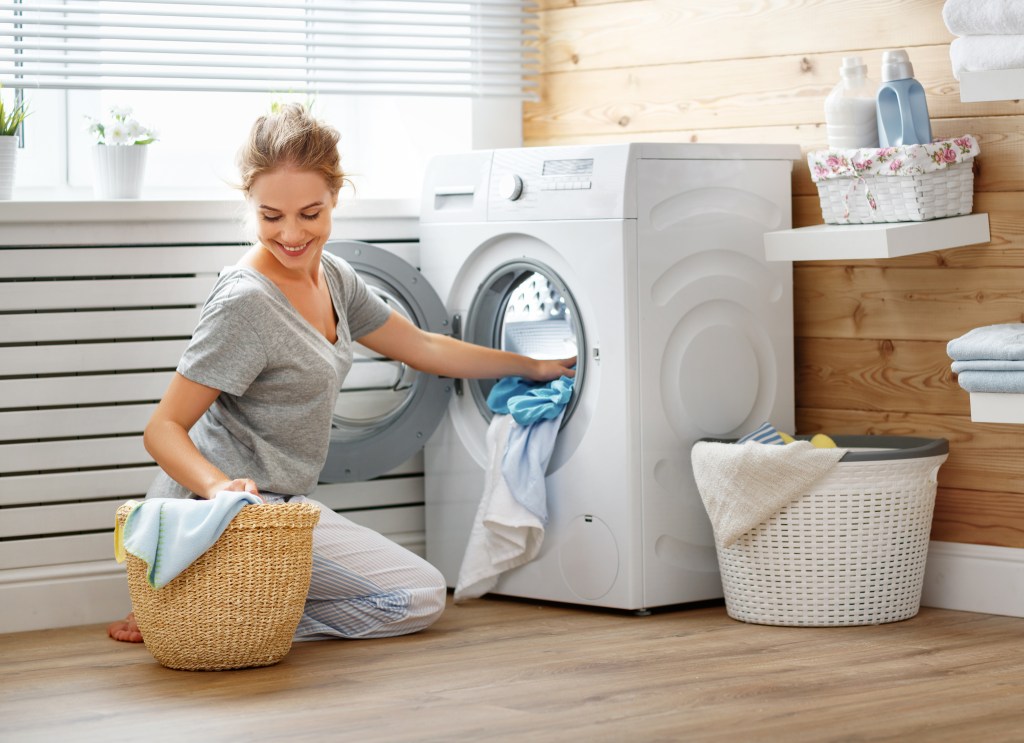 A happy woman in a laundry room loading a washing machine.