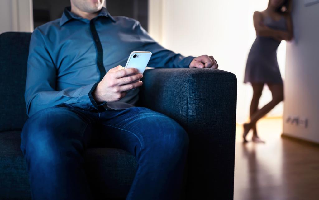 Cheater man using phone next to jealous wife peeking and suspicious, in infidelity, jealousy, and betrayal scene.