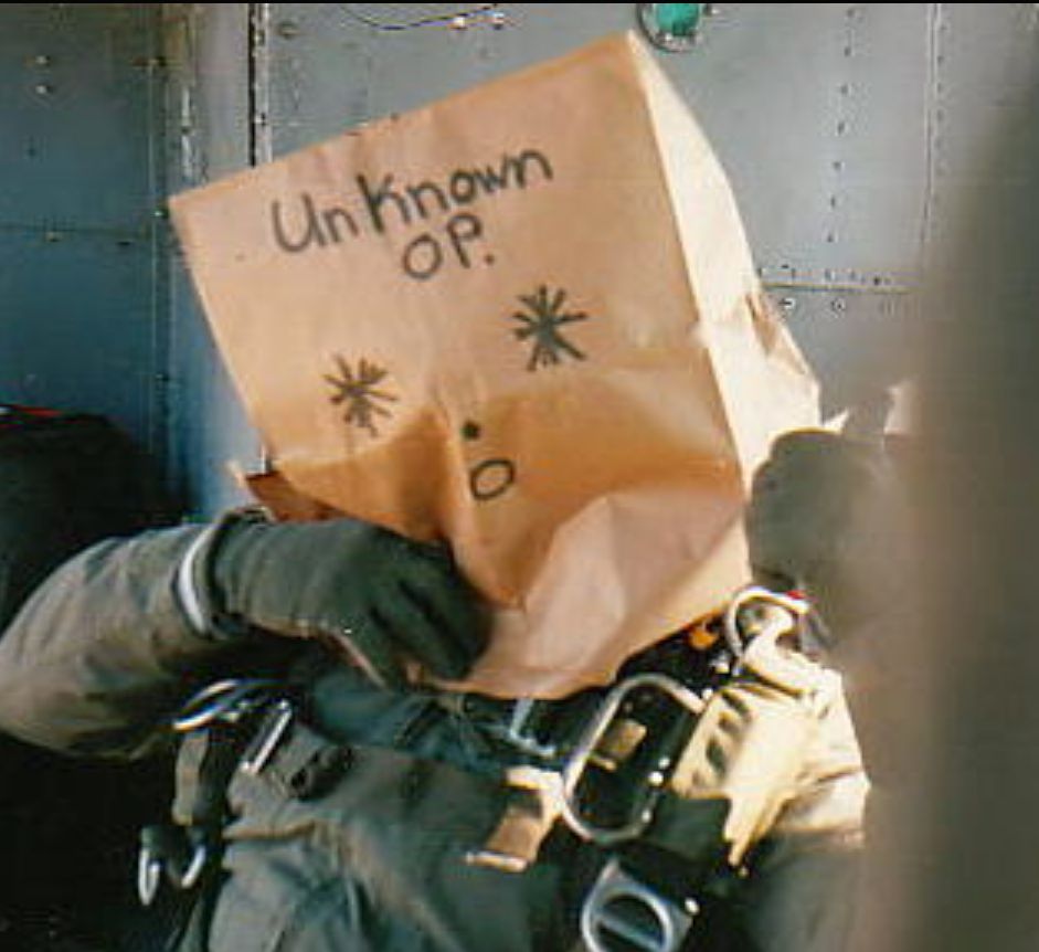 Military person with a brown paper bag over their head. The bag reads "Unknown Op." 