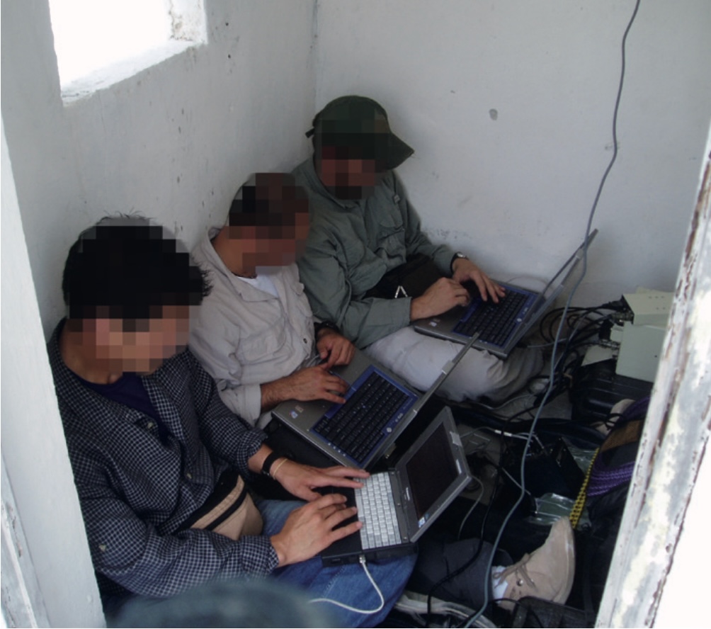 Three men with blurred faces in a cramped space type on computers. 