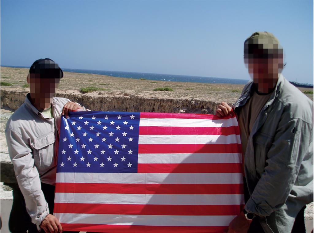 Two men, with faces blurred, hold an American flag off the coast of Africa. 