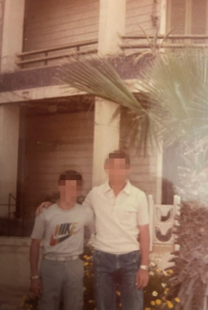 Adam Gamal, as a young boy, and his father standing with their arms around each other. Both have their faces blurred out. 