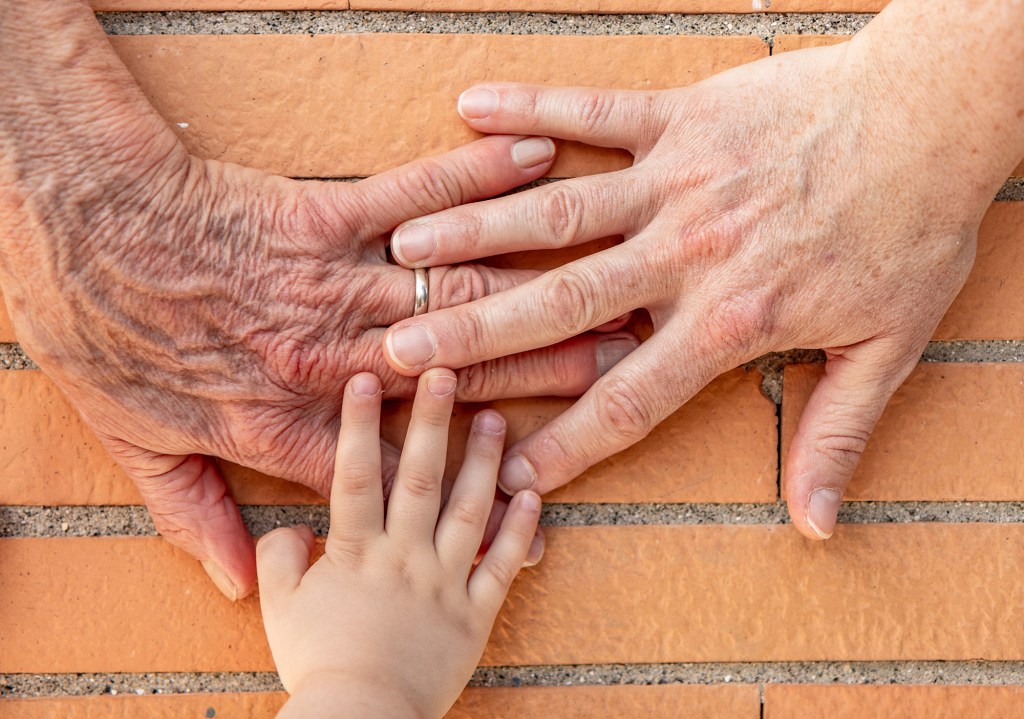 Three hands, one elderly woman, one woman, one girl. Family unity, love, help, assistance.