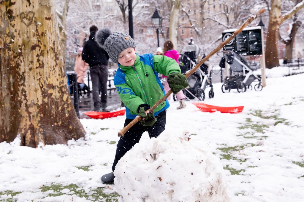 Boy playing in snow in Washington Square park building snowman