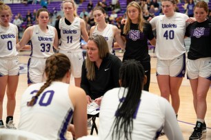 Meg Barber coaches in the huddle during an NYU women's basketball game.