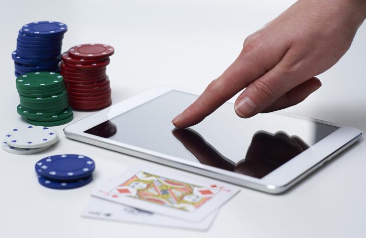 person using a tablet surrounded by two playing cards and poker chips