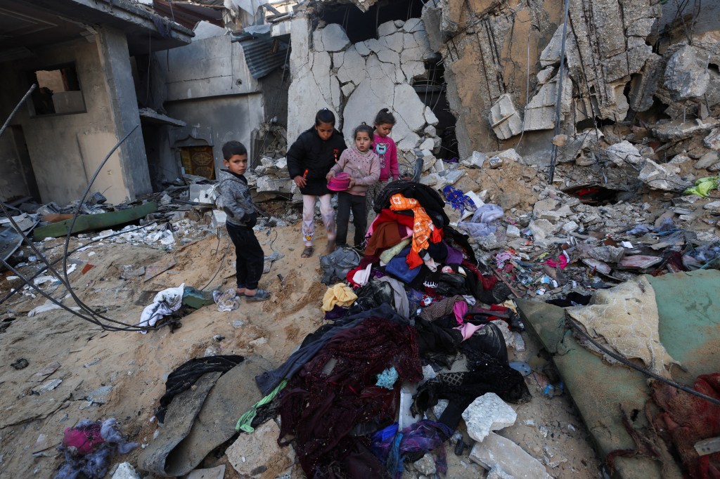 Palestinian children stand near a pile of clothes amid rubble at the site of an Israeli strike.