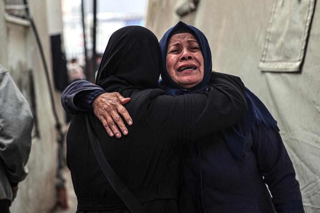 Two women wearing black clothing and head coverings embrace in tears amid the bombardment in southern Gaza.