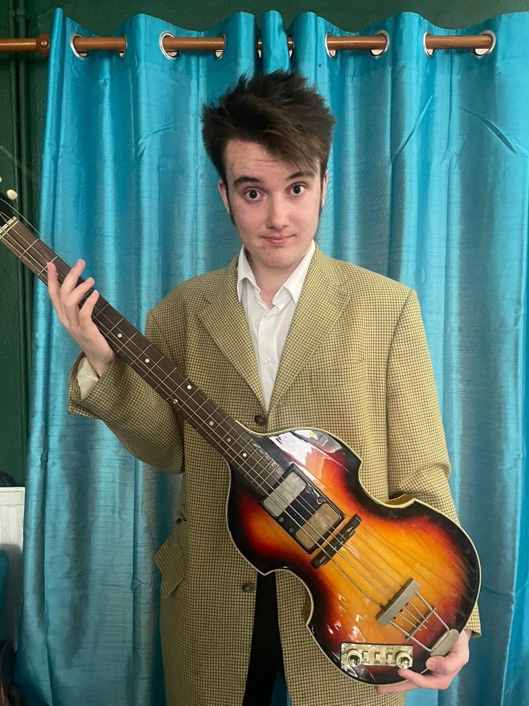 Paul McCartney's legendary stolen bass guitar, found after 50 years, held by Ruaidhri Guest with a cheeky expression.