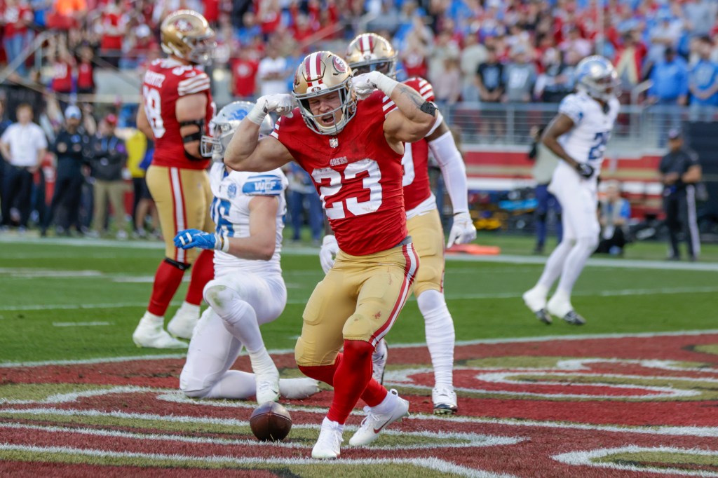 Christian McCaffrey scoring a touchdown in a red uniform during the football game between Lions and 49ers.