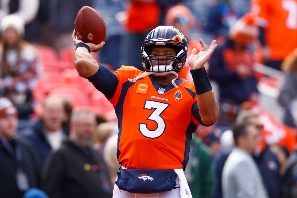 Russell Wilson holding a football while warming up before a game between Denver Broncos and Los Angeles Chargers at Empower Field at Mile High.