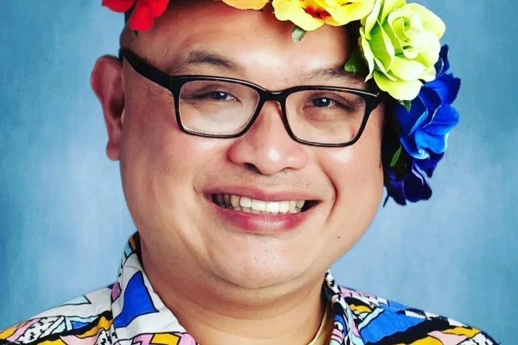 Science teacher Rachmad Tjachyadi in headshot in front of blue background wearing flowery headpiece and brightly colored printed shirt, smiling with glasses