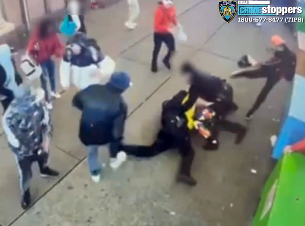 A group of migrants attack an NYPD officer on a sidewalk at night.