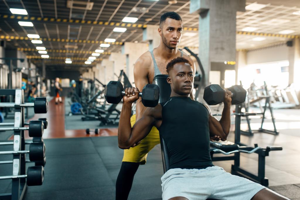 Two men lifting dumbbells on bench in gym.