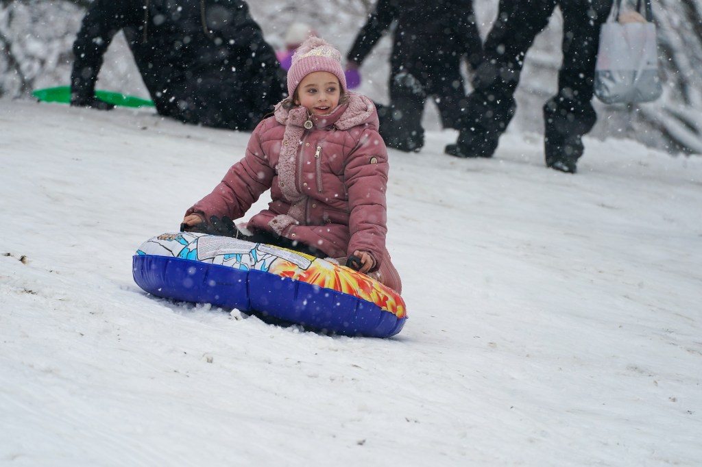 a girl sledding down a hill in the snow, Turkey Hill, Central Park, NYC, enjoying the snow and outdoors, on what would have been an in school day. Snowfall continues today.