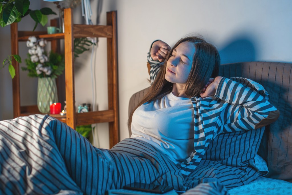 A young woman stretching and preparing for bedtime in her cozy bed.