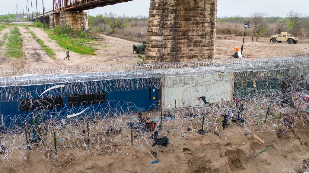 In an aerial view, a Texas National Guard soldier walks past a barrier of shipping containers and razor wire at he U.S.-Mexico border in Eagle Pass, Texas. 