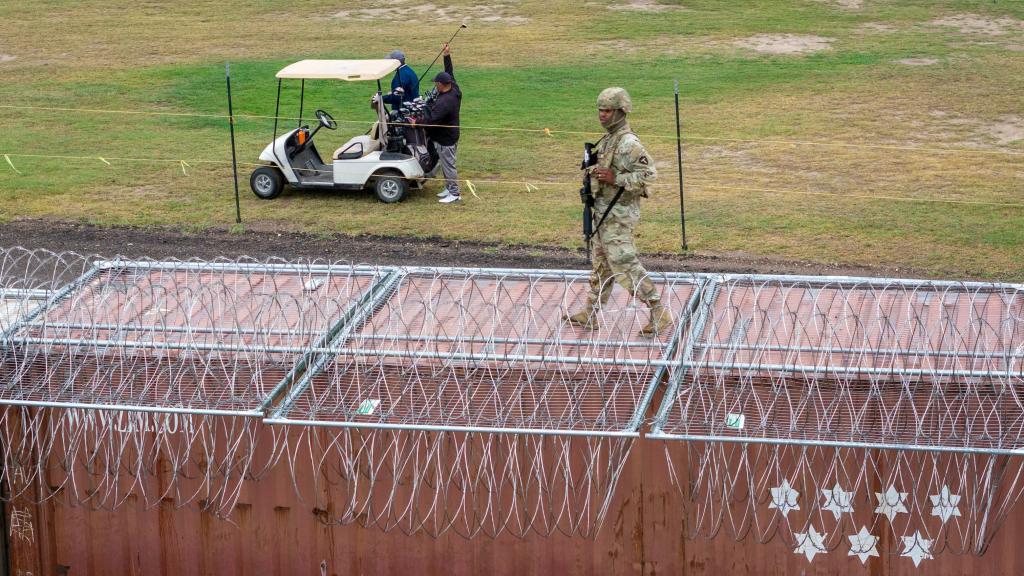 In an aerial view, a Texas National Guard soldier stands atop a barrier of shipping containers and razor wire while guarding the U.S.-Mexico border