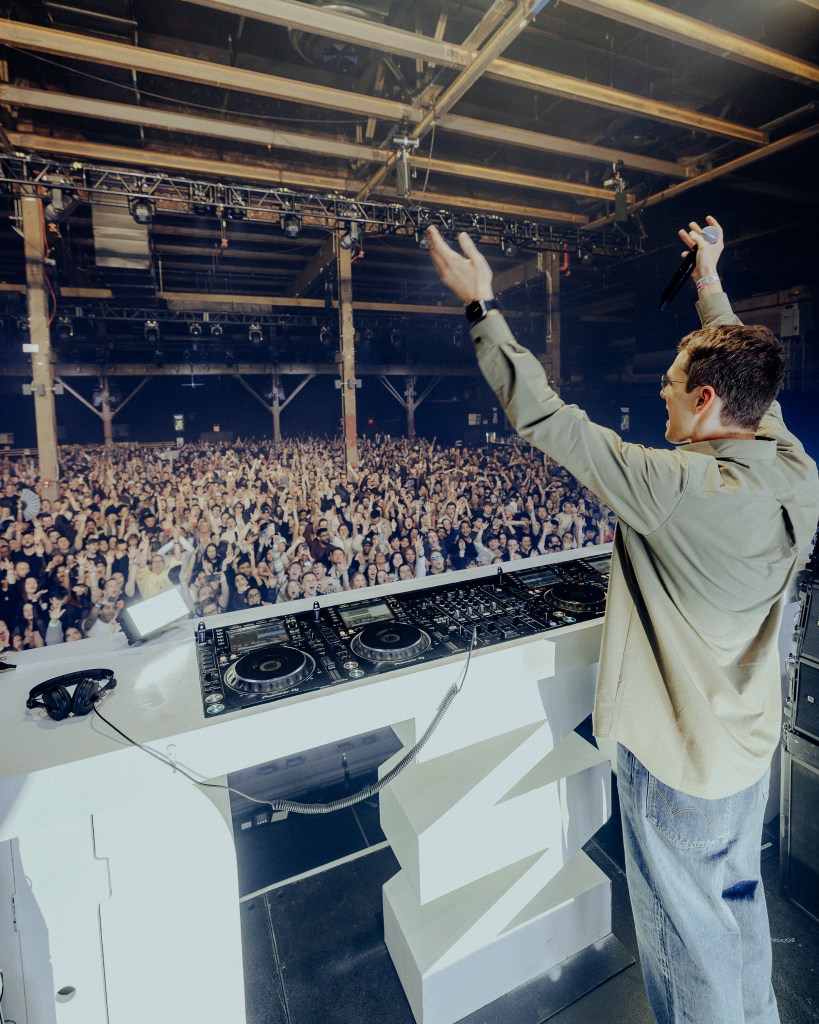 Man holding microphone on stage with large crowd.