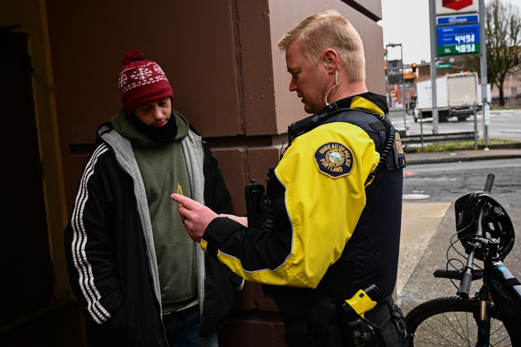 Portland Police Officer Eli Arnold issues a citation for drug use while also handing the man a business car for health screening and services to avoid a $100 fine in Portland on Jan. 25, 2024. 