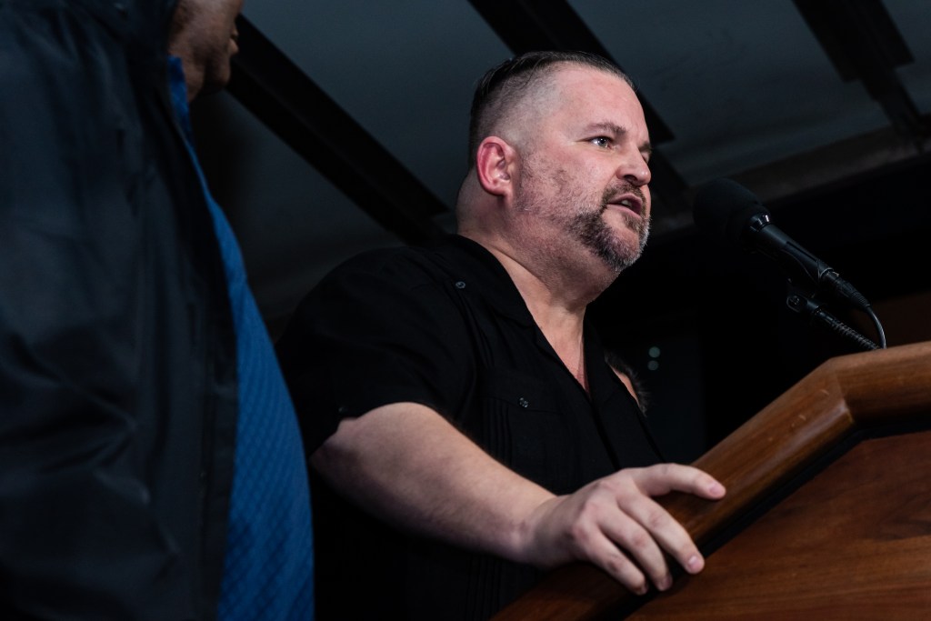 John Samuelsen addressing a rally outside MTA headquarters, standing at a podium with a microphone.