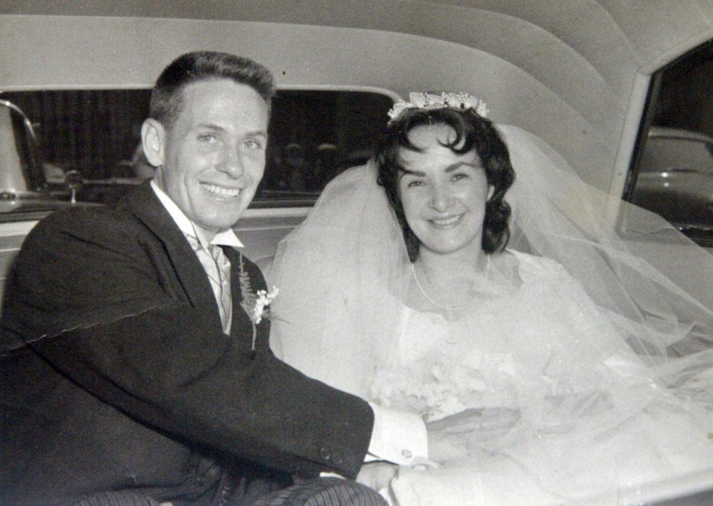 A man and woman sitting in a car on their wedding day in 1960.