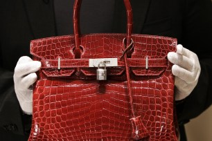 A person holding a red Hermes Birkin Bag made of crocodile leather.