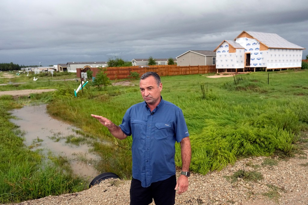 Developer Trey Harris talks about the Colony Ridge development as he stands near a near home under construction next to a row of mobile homes 