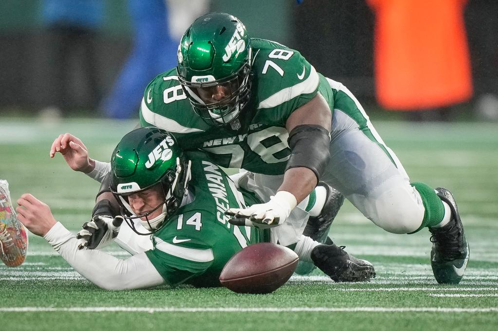 Two NFL players in green uniforms on the field during a game, one recovers a fumble while the other watches. (AP Photo/Bryan Woolston, File)