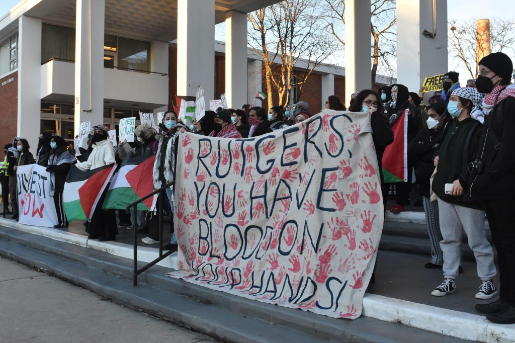 Protesters at Rutgers University holding a banner says, "Rutgers, you have blood on your hands!" along with Palestinian flags and a second banner that says, "Divest Now."