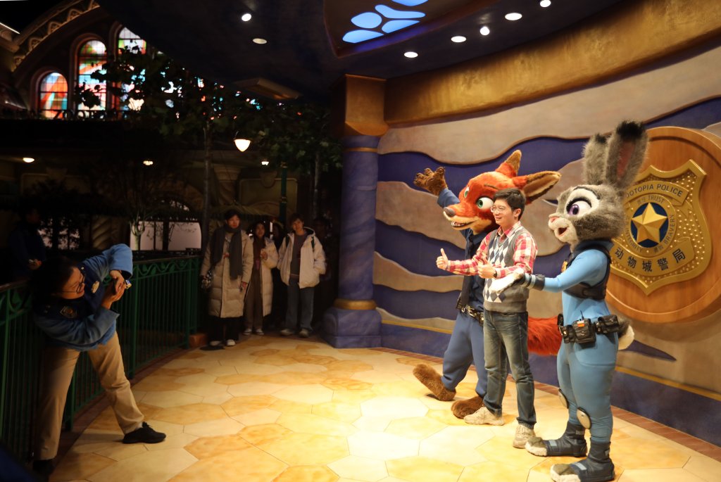 A visitor poses with staff members in costumes from film "Zootopia" at Shanghai Disney Resort, surrounded by others in clothing.