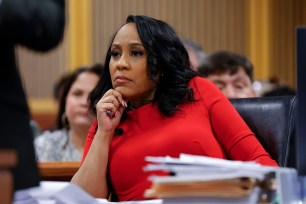 A woman in a red dress sitting in a chair with a pile of papers in front of her, during a hearing at the Fulton County Courthouse in Atlanta.