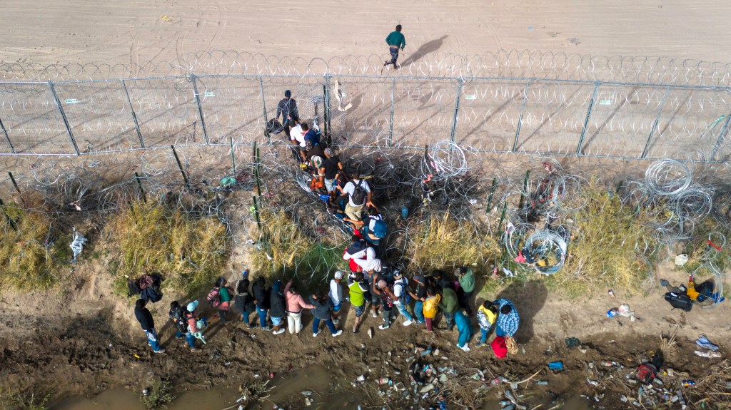 In an aerial view, immigrants pass through coils of razor wire while crossing the U.S.-Mexico border on March 13, 2024 in El Paso, Texas. 